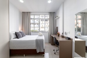 Habitación de hotel con cama, escritorio, silla, espejo y ventana con cortinas.