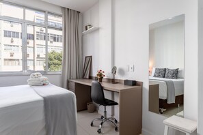 Habitación de hotel con cama, escritorio, silla, espejo y ventana con vistas a edificios.
