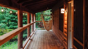 A wooden porch with a hammock, wooden railings, and a view of greenery.