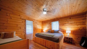 A wooden-paneled bedroom with a bed, bedside tables, and a ceiling fan.