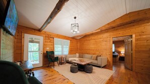 A cozy log cabin interior with a sofa, chairs, a coffee table, and a television.