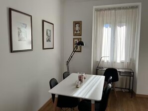 Ein Zimmer mit weißem Tisch, schwarzen Stühlen, einem Schreibtisch mit Computer und gerahmten Bildern an der Wand.