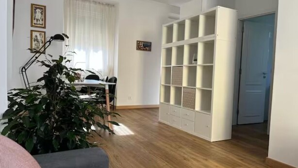 Un salon spacieux doté d’un plancher en bois, d’une bibliothèque blanche et d’un coin repas avec une table et des chaises.
