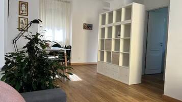 Ein geräumiges Wohnzimmer mit Holzboden, einer weißen Regaleinheit und einem Essbereich mit Tisch und Stühlen.