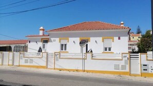 Un bâtiment blanc avec un toit recouvert de tuiles rouges, des éléments décoratifs jaunes et une entrée fermée par un portail.