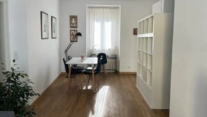 Une pièce avec un plancher en bois, une table à manger avec des chaises, un lampadaire et une fenêtre avec des rideaux.