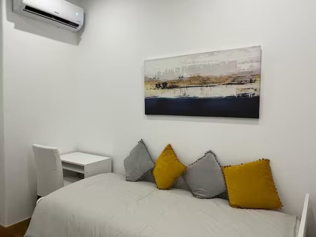 Ein Schlafzimmer mit Bett, Schreibtisch, Klimaanlage und einem Bild an der Wand.