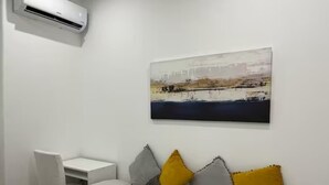 Une chambre avec un lit, un bureau, un climatiseur et un tableau au mur.