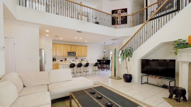 A spacious living area with a white sofa, a coffee table, and a TV. A kitchen is visible in the background, and there is a staircase leading to an upper level. - Rosey Bouldin Home + Minutes to DT - Adelaide! (Austin)