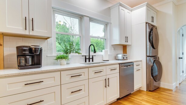 A modern kitchen with white cabinetry, a coffee maker, a sink, a dishwasher, and a built-in oven.