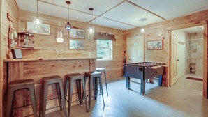 Een gezellige kamer met houten wanden, een tafelvoetbaltafel en barstoelen.