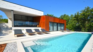 A modern poolside area with a rectangular pool, sun loungers, and a contemporary building with large windows. - House K2 (Kanfanar)