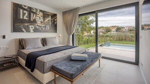 A modern bedroom with a large bed, a bench, a view of a swimming pool, and a cityscape through large windows. - House K2 (Kanfanar)