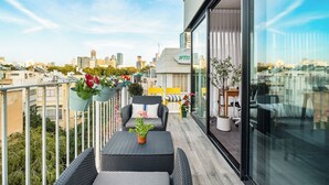 A balcony with wicker furniture, potted plants, and a city view. - Top TLV Grand Suites (Tel Aviv)