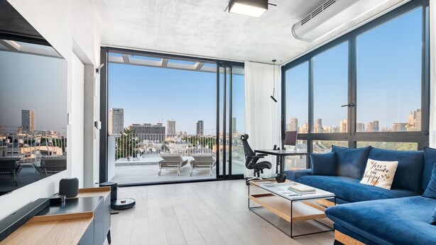 A modern living room with a city view, a blue sofa, a coffee table, and a desk with a computer. - Top TLV Grand Suites (Tel Aviv)