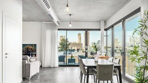 A modern living space with a dining area, large windows, and a view of the cityscape. - Top TLV Grand Suites (Tel Aviv)
