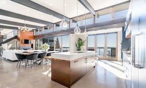 A modern kitchen with a central island, large windows, and a view of the outdoors. - Luxury Muskoka Waterfront Cottage | 5BR | Sauna, EV Charger. Sleep 12 (Port Severn)