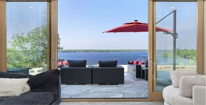 A modern outdoor seating area with a view of a lake. - Luxury Muskoka Waterfront Cottage | 5BR | Sauna, EV Charger. Sleep 12 (Port Severn)