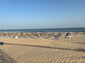 A beach with rows of sun loungers and umbrellas, a wooden walkway, and a clear view of the ocean. - Casita en Aldea de Pescadores, en Medio del Pinar y la Playa. Olvídate del Coche (Monte Gordo)