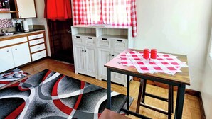 A compact kitchen with a microwave, sink, and a red curtain. There's a checkered table with two salt shakers and a bench. - Stay right in the heart of Long Beach, WA — steps from the ocean! (Long Beach)