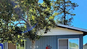 A single-story house with a gray exterior, a visible number '119' on the side, and a tree in front. - Stay right in the heart of Long Beach, WA — steps from the ocean! (Long Beach)
