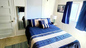 A bedroom with a bed, a nightstand, a lamp, a window with curtains, and a door. - Stay right in the heart of Long Beach, WA — steps from the ocean! (Long Beach)