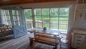 Une cuisine chaleureuse, dotée de meubles en bois, de grandes fenêtres et offrant une vue sur une terrasse et la verdure environnante.