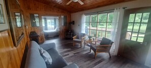 A cozy cabin interior with a wooden floor, a sofa, wicker chairs, a table, and a fireplace.