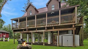 A two-story house with a balcony, a fire pit, and a grill area. - Riverfront Retreat For Kayaking, Fishing and Hot Tub (Falls)