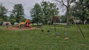 A playground with swings and slides, surrounded by trees and grass.