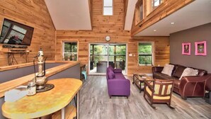 A wooden interior with a purple sofa, a brown leather sofa, and a dining area with a table and chairs. - Riverfront Retreat For Kayaking, Fishing and Hot Tub (Falls)