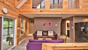 A wooden cabin interior with a loft bedroom, a living area with a sofa and coffee table, and a kitchen with a refrigerator. - Riverfront Retreat For Kayaking, Fishing and Hot Tub (Falls)