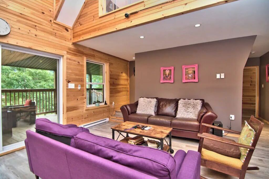 Un intérieur en bois avec un canapé en cuir marron, des fauteuils violets et une table basse en bois.