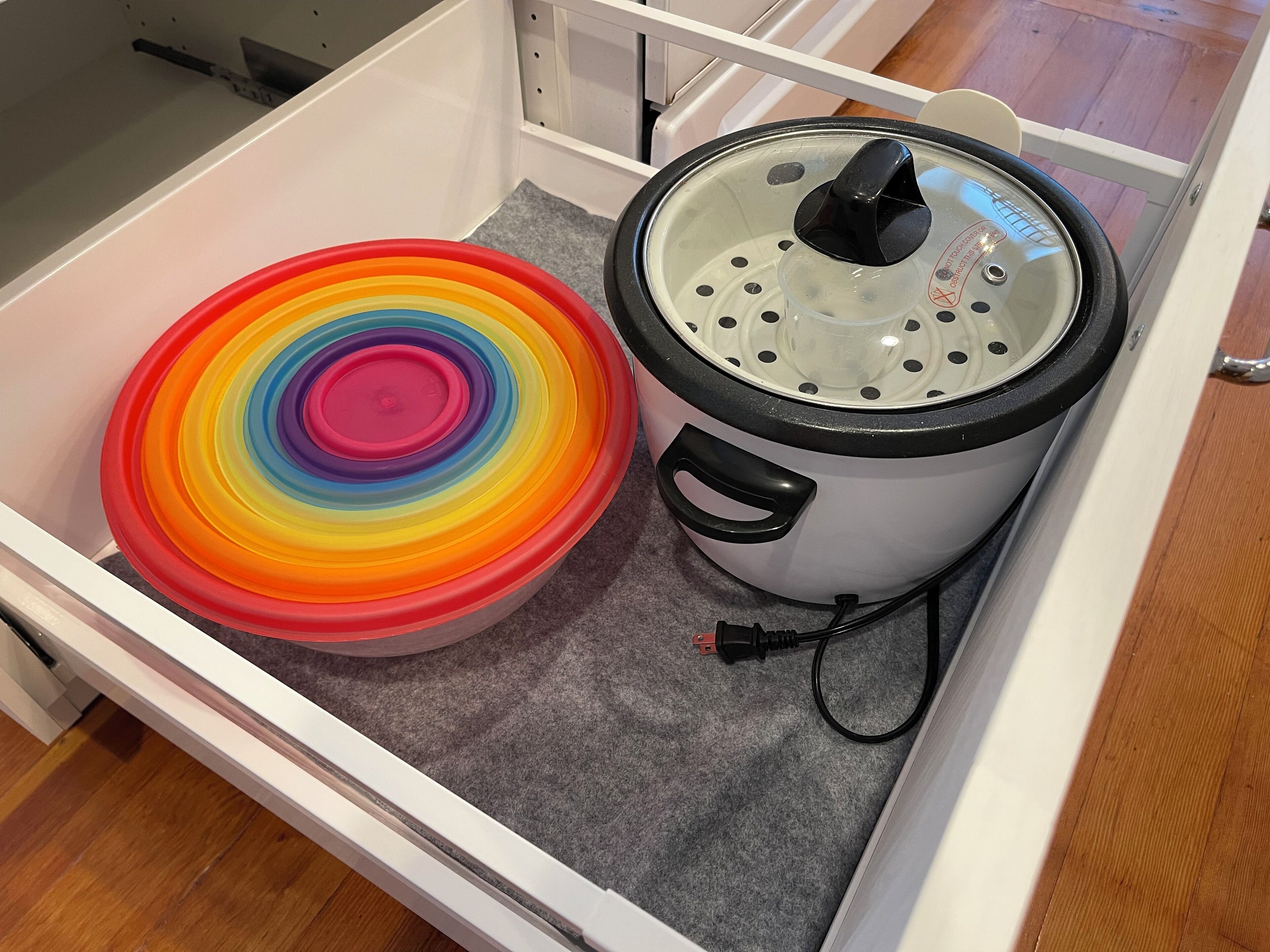 A kitchen drawer containing a rice cooker and a colorful container.