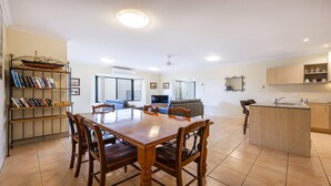 Uma sala de estar ampla com uma mesa de jantar, cadeiras, sofá, televisão e estante de livros.