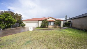Um imóvel residencial com garagem, um jardim frontal com grama e um muro de tijolos.