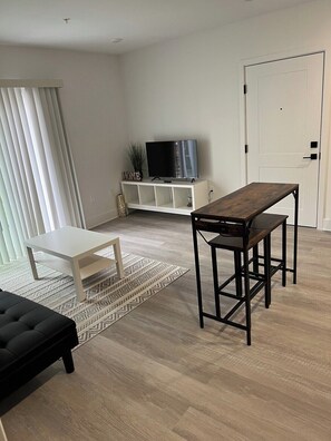 Un salon moderne avec une table basse en bois, un canapé blanc, un téléviseur posé sur un meuble blanc et un tapis à motifs.
