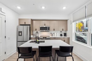 A modern kitchen with a central island, stainless steel appliances, and a view of the city through large windows. - Brookland Getaway Steps from Shops & Dining (Washington)