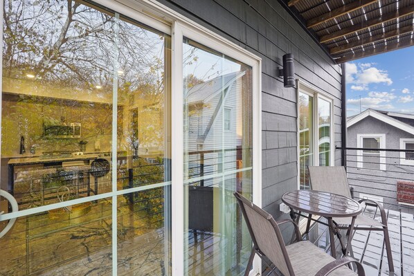 A covered outdoor seating area with a table and chairs, large glass windows, and a view of a building with a staircase. - Stylish 1BD Brookland Home with Great Views! (Washington)