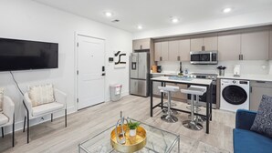 Cuisine moderne équipée d’un four à micro-ondes, d’un réfrigérateur et d’un lave-linge. Un coin repas avec une table et des tabourets de bar est également disponible. Un téléviseur à écran plat est fixé au mur.