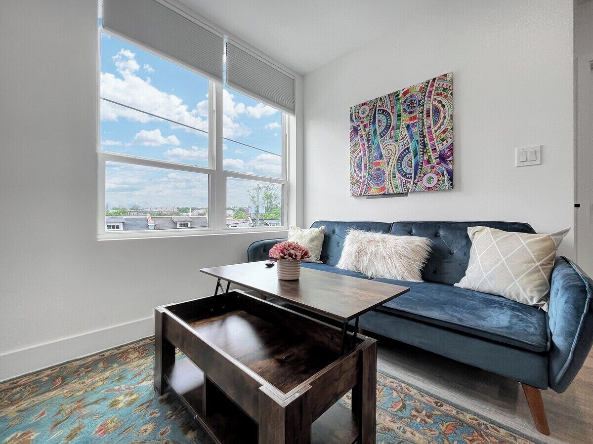 A modern living room with a blue sofa, a wooden coffee table, and a colorful abstract painting on the wall.
