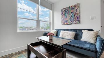 A modern living room with a blue sofa, a wooden coffee table, and a colorful abstract painting on the wall.