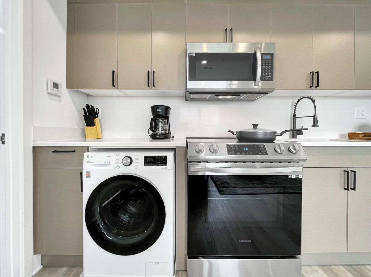 A modern kitchen with a washing machine, oven, microwave, and coffee maker.