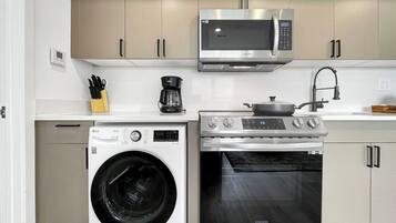A modern kitchen with a washing machine, oven, microwave, and coffee maker.