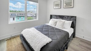 A modern bedroom with a large bed, a view of the city through large windows, and two framed pictures on the wall.