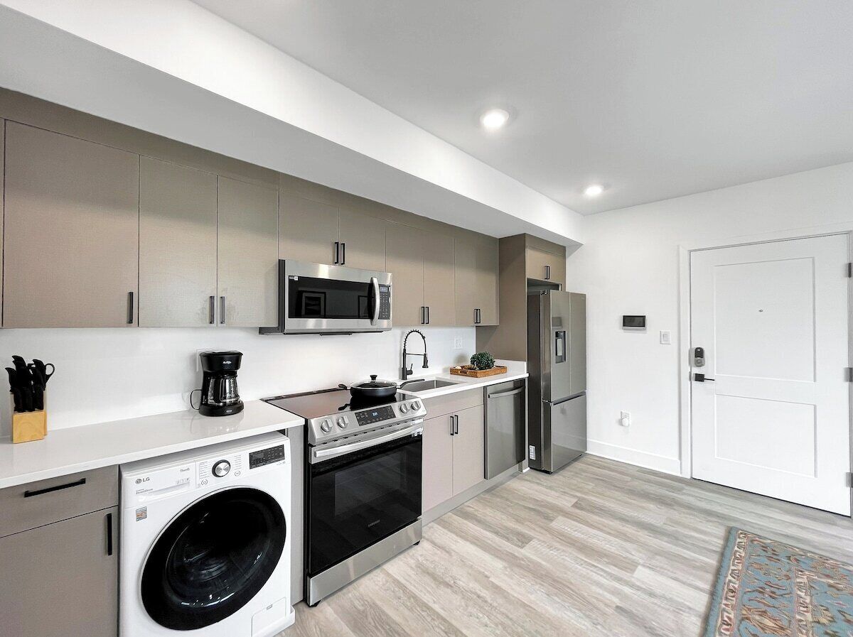 A modern kitchen with a washing machine, microwave, stove, and refrigerator.