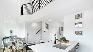 Eine moderne Küche mit einer zentralen Kochinsel, ein Essbereich mit Glastisch und eine Treppe, die in einen oberen Bereich führt.