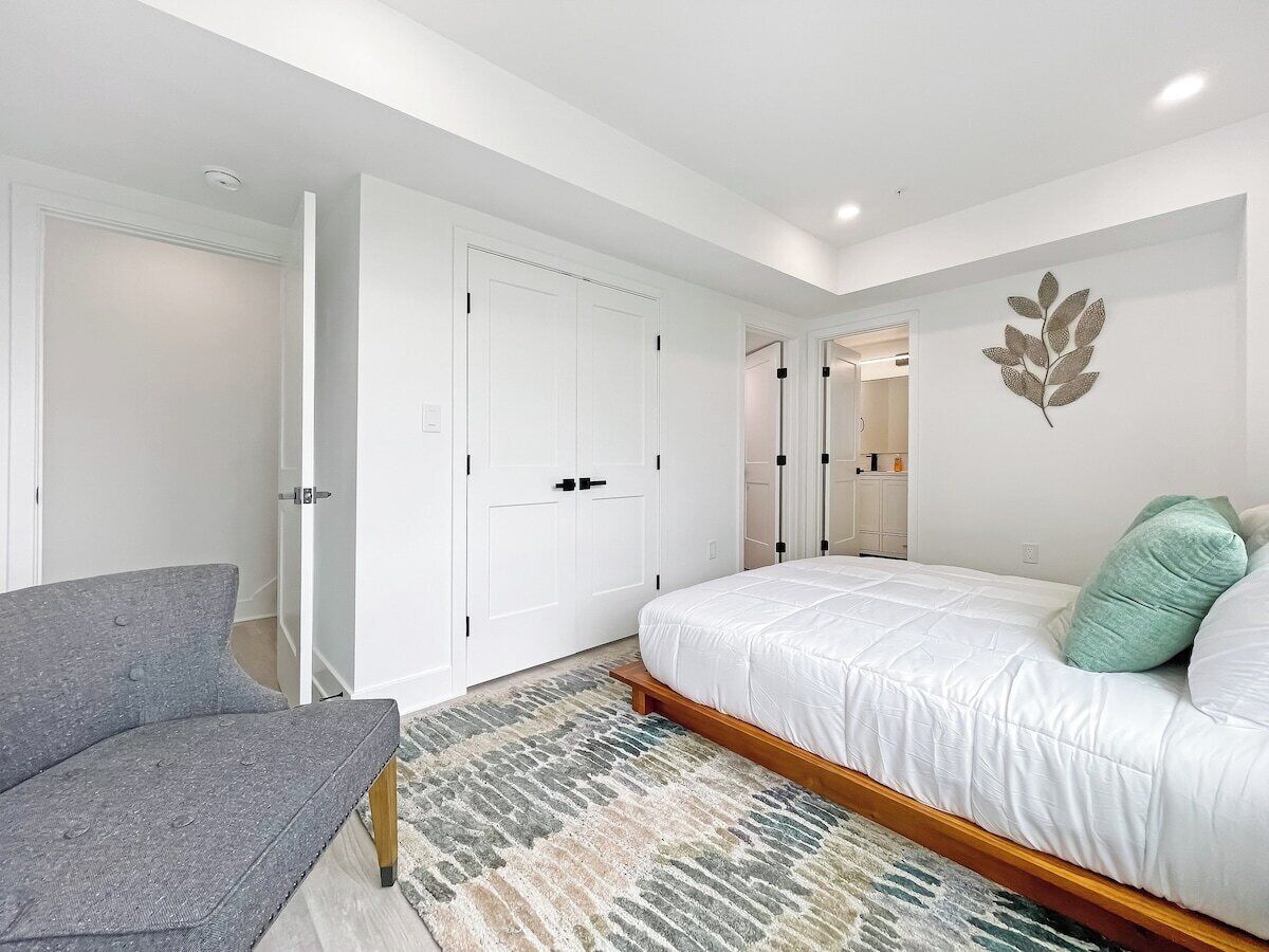 Un dormitorio con una cama, una silla gris, un armario blanco y un espejo.
