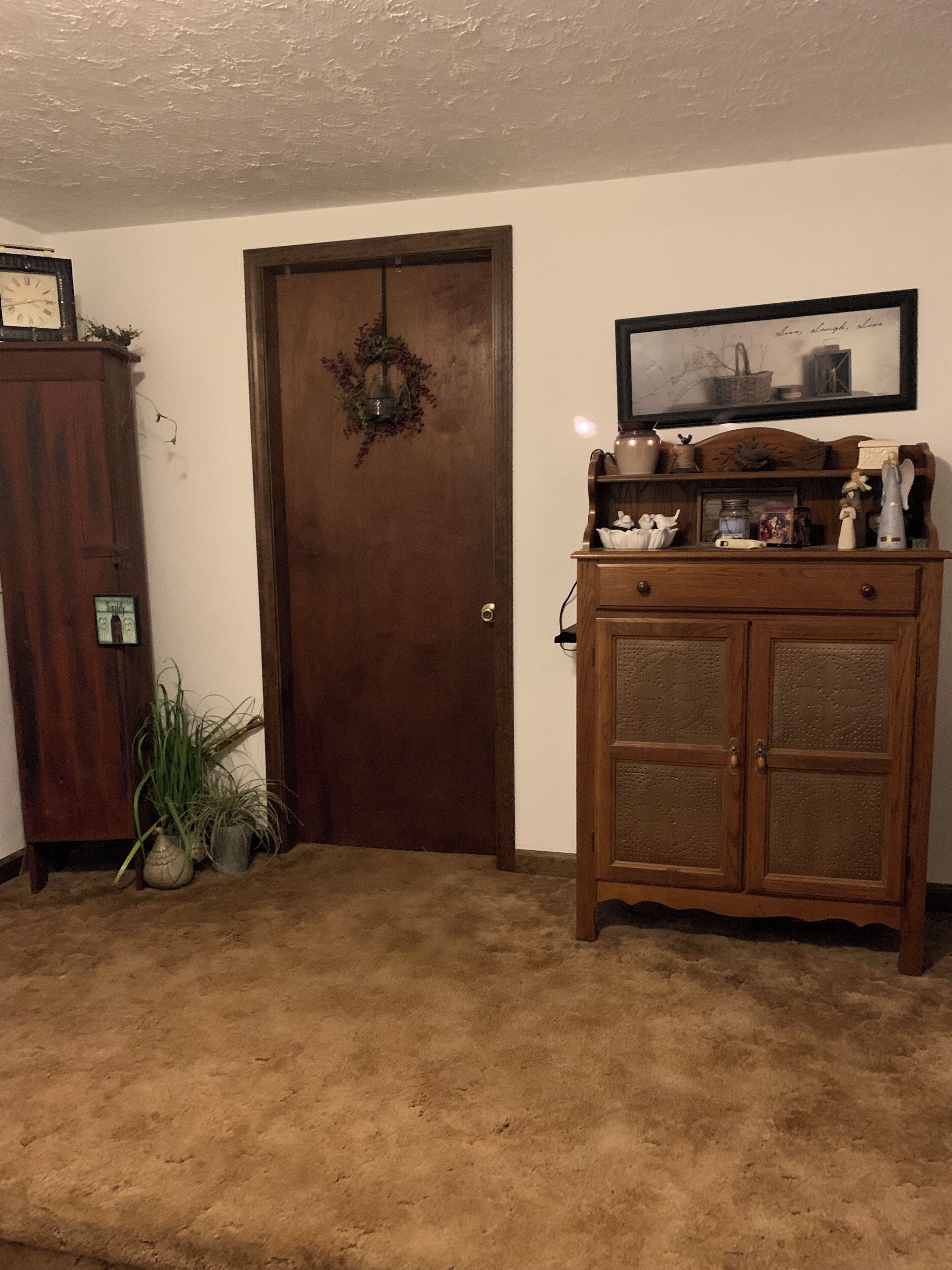 A room with a wooden door, a small cabinet with decorative items, and a framed picture on the wall.