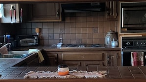 A kitchen with wooden cabinets, a microwave, a toaster, and a bar area with stools.